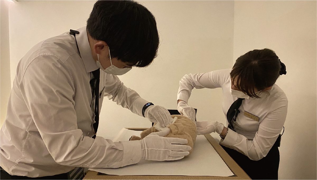장례지도사 두 명이 흰 장갑을 끼고 염습하는 모습
